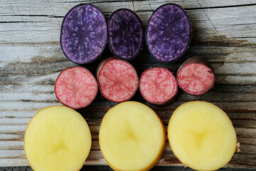 Cross-sections of yellow, purple and pink potatoes arranged on rustic wood, showcasing a variety of bright colors and smooth internal textures.