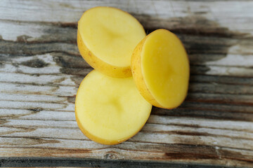 Three yellow potato slices arranged on a rustic wooden surface, showcasing their smooth texture and golden color with copy space.