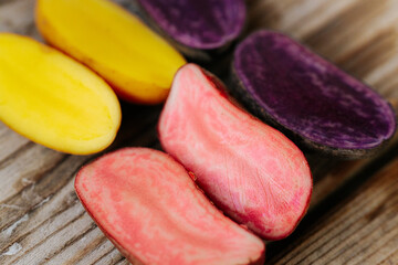 Six potato halves in bright yellow, pink and purple tones arranged on a wooden surface, showcasing...