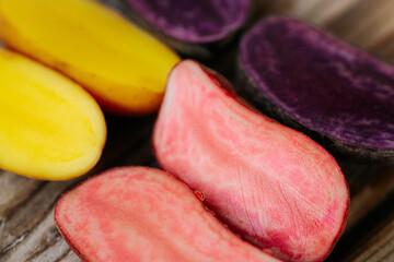 Six potato halves in bright yellow, pink and purple tones arranged on a wooden surface, showcasing their inner diversity. Space for text included.