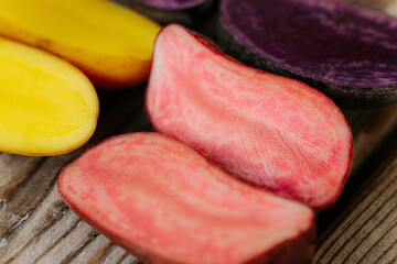 Six potato halves in bright yellow, pink and purple tones arranged on a wooden surface, showcasing...