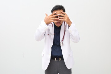 Asian adult male doctor on isolated white background, peeking in shock while covering face and eyes...