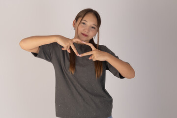 A young, smiling woman with long brown hair stands against a plain light background, looking...