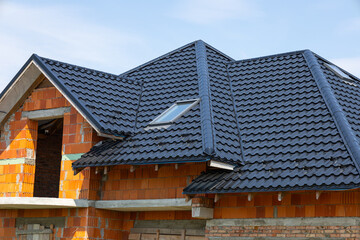 Construction of a house with a black tiled roof and orange brick walls in the framework stage during bright daylight