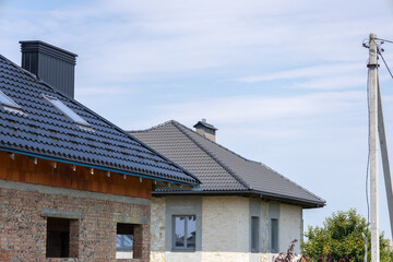 Two houses in various stages of completion are situated in a peaceful suburban area, featuring a blue sky overhead and power lines nearby
