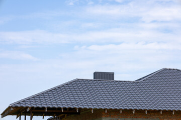Construction workers are installing a modern roof with textured shingles on a house while the sky...