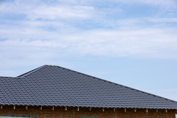 Fototapeta premium A detailed view of a textured roof under a clear blue sky with scattered clouds reveals the intricate patterns of the tiles