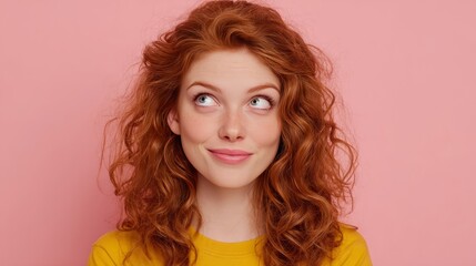 Naklejka premium A captivating woman with fiery red, curly hair looks upwards, a playful, and contemplative expression, against a soft pastel backdrop.