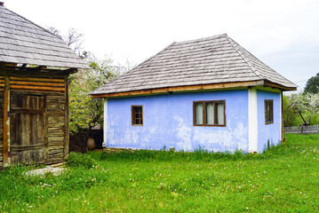 Blue painted traditional Romanian house with a cozy green courtyard and wooden outbuildings at...
