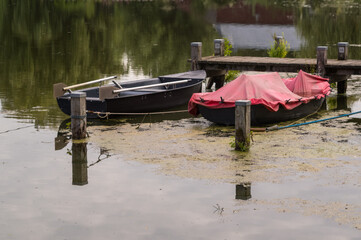 Two boats moored at wooden dock on calm lake covered with duckweed