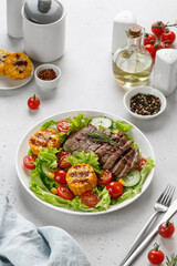 Roast beef salad on white plate and grey background. Salad, meal with meat steak, grilled corn and beef meat with vegetable. Diet dinner concept.