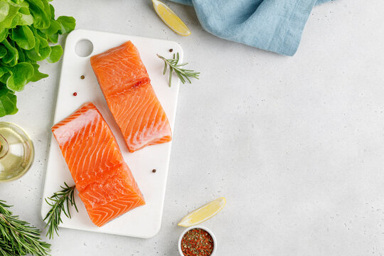 Salmon. Fish steaks, slices. Raw uncooked salmon fillet fish with rosemary, lemon and pepper on white cutting board and grey background.