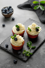 Cupcakes, muffins decorated with cream, berries and green mint leaves on dark slate cutting board. Delicious homemade dessert. Pastry.