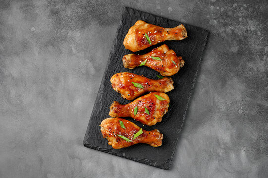 Roasted Baked chicken legs drumsticks on black slate board on dark background. Meal, dinner diet concept, diet. Copy space for text.