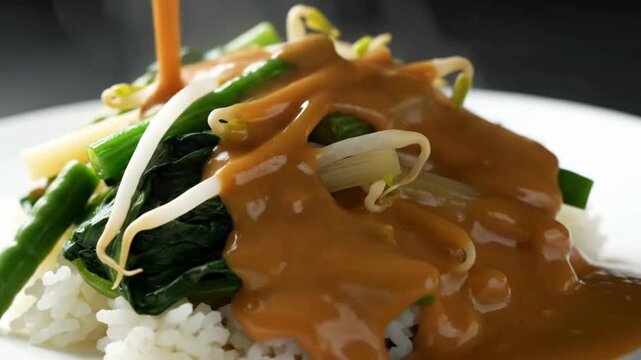 Peanut sauce is poured over a plate of steamed vegetables and rice, a delicious and healthy meal. pecel