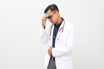Asian male doctor standing wearing doctor's coat, stethoscope on neck, gesturing headache,...