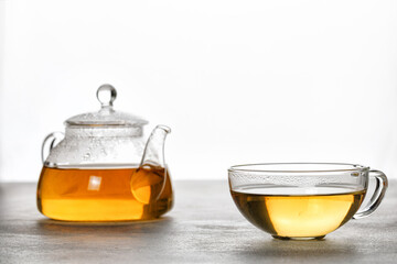 A mug or cup with green herbal tea and a teapot with tea leaves on grey background. Beauty color