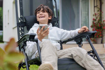 Young boy enjoying screen time in comfortable outdoor lounge chair at home. childhood, digital...