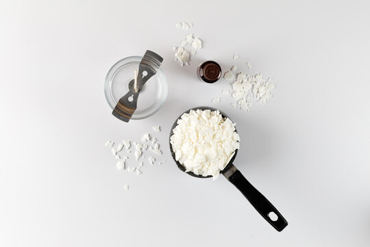 Equipment for candle making with white soy wax flakes, fragrance and jar with wick. Flatlay, top view. White background
