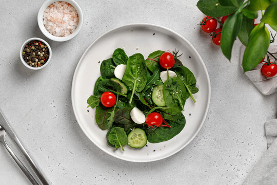 Fresh green salad leaves with arugula, spinach, cucumber, cherry tomatoes, mozzarella on grey background.