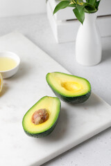 Cut ripe green avocado on a white marble board with vase and lemon juice. Food composition.