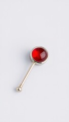 Close-up of polished silver object with rounded tip and cabochon red gemstone on light gray background, soft light, minimalist and elegant design.

