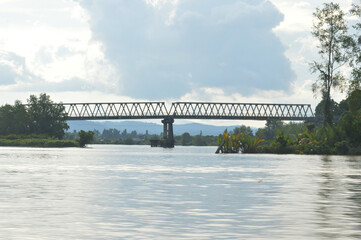 Steel bridge stretches over a river, connecting a lush landscape under cloudy skies