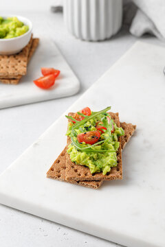 Sandwich with avocado paste on bread with tomatoes cherry and arugula on white table. Light photography