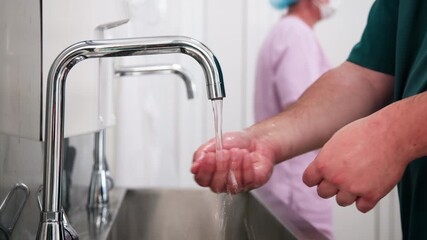 Close-up of hands with soap under running water. A healthcare worker washes hands in a hospital. Concept of hygiene and preparation for work. - Powered by Adobe