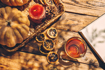 Cozy warm autumn composition with cup of hot tea, burning candle, open book and pumpkins on wooden...