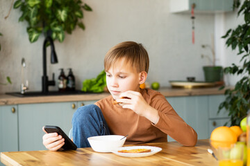 Cute blonde teenager boy have breakfast holding a glass of orange juice at home in the kitchen....