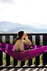 Young woman relaxing in hammock on balcony with mountain view.