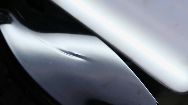 Small thin dent on special surface of smooth automobile body. Unevenness provides evidence car comes into contact with sharp object