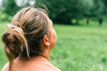 Mature woman enjoying nature in lush green field. Standing with her back to camera and looking at...