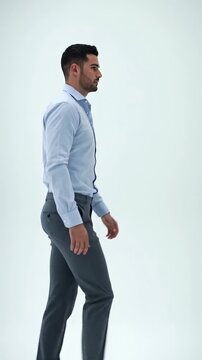 Confident young man in light blue shirt and grey chinos strides purposefully through a vast, brilliantly illuminated pure white abstract space. A low-angle 9:16 vertical video emphasizing his