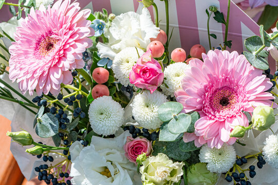 Bright floral bouquet with pink gerbera daisies, roses, white chrysanthemums, and berries. Festive and elegant flower arrangement in natural light.
