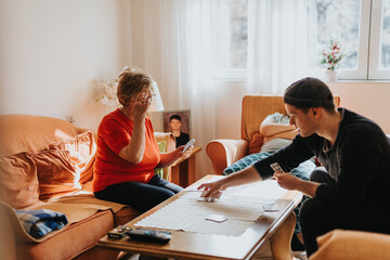 A warm moment where an elderly woman and a young man enjoy a card game together at home, surrounded...