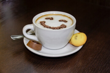 Obraz premium A cup of coffee with candy and biscuits on dark background. Smile is depicted on the coffee from the foam. Coffe - smile