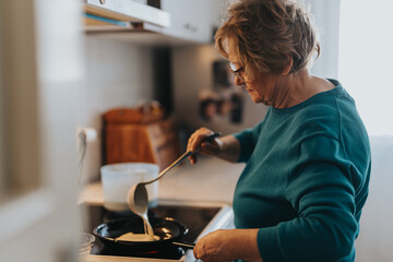 An elderly woman wearing glasses and a blue sweater is carefully preparing food in a warm, well-lit kitchen, reflecting homely comfort and culinary tradition.