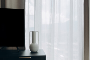 Modern home interior with television and minimalist decor on cabinet. Vase and curtains add visual...