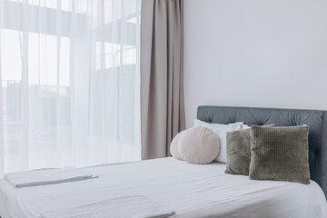 Daylight floods elegant bedroom with neutral curtains and plush cushions arranged symmetrically....