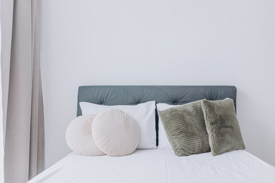 Simple bedroom interior with textured cushions, soft bedding, and fabric headboard. Beige curtain frames the space, emphasizing order and softness.Symmetrical arrangement of decorative pillows on soft