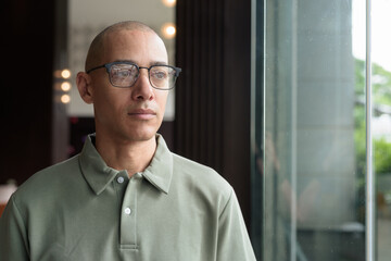 Bald Hispanic man looking through window in hotel lobby with eyeglasses, stylish confident portrait