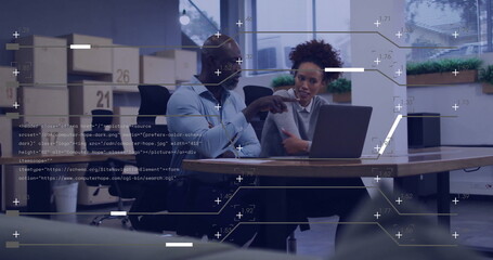 Pointing man guiding coworker at office conference table, with laptop, boxes notebook and plants