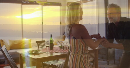 Dancing mature couple wearing striped dress, dark shirt in dining area at sunset, with wine bottle