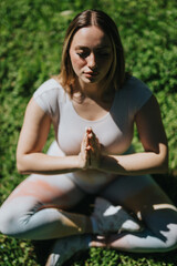 A woman focusing on meditation while seated outdoors on grass, embodying relaxation, mindfulness,...