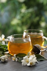 Tasty jasmine tea in cups, dry leaves and flowers on black table, closeup