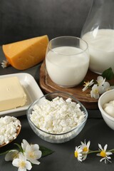 Fresh dairy products and flowers on grey wooden table against dark background