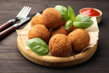Delicious fried croquette balls with basil on wooden table, closeup