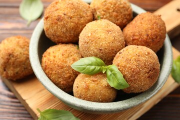 Delicious fried croquette balls with basil in bowl on wooden table, closeup
